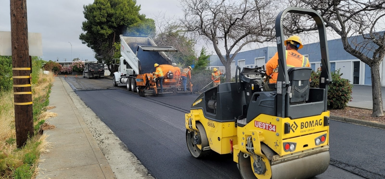 paving company laying asphalt for new road and smoothing with roller